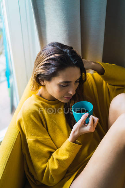 Vista ad angolo basso di donna sognante seduta con tazza in poltrona — Foto stock