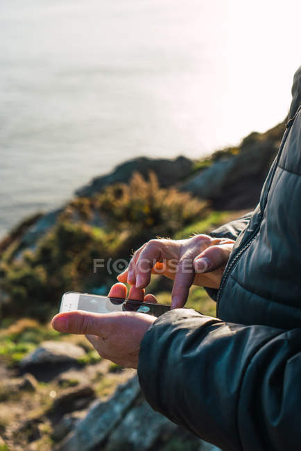 Crop man using smartphone on coastal hill — Stock Photo