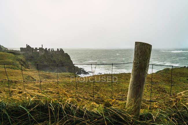 Vista a la valla y verdes rocas costeras en la orilla del océano - foto de stock