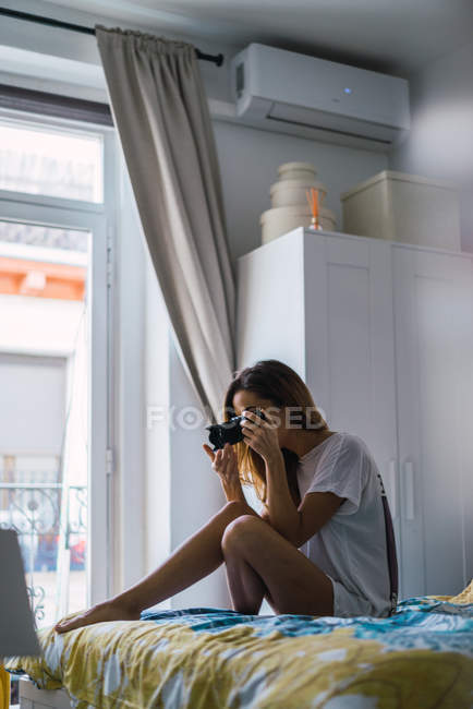 Vista lateral da mulher sentada na cama e tomada de tiro com câmera — Fotografia de Stock