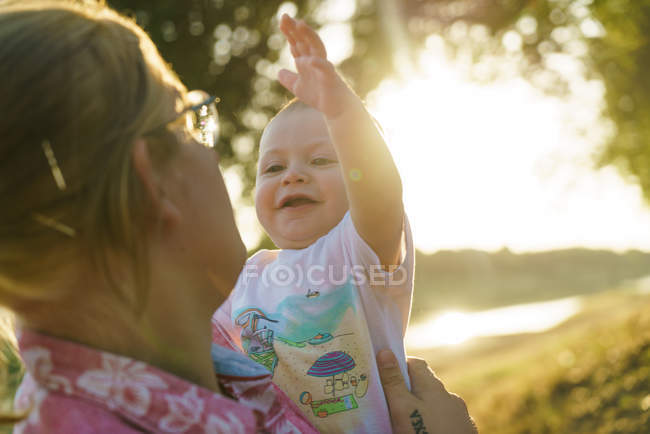 Porträt eines fröhlichen Kindes an den Händen der Mütter im Park — Stockfoto