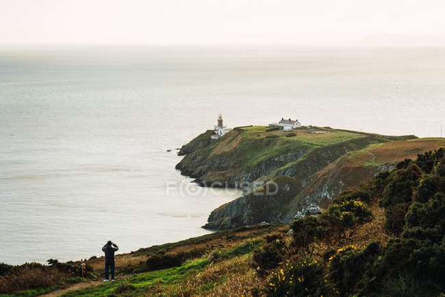 Vue lointaine du touriste debout sur la côte rocheuse couverte d'herbe . — Photo de stock