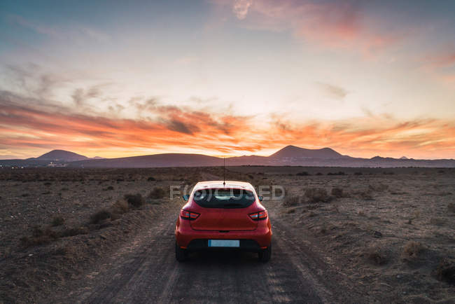 Задній вид червоний автомобіль припаркований на сільській дорозі, що веде до гори у вечорі — стокове фото