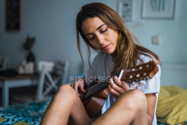 Портрет женщины, сидящей на кровати и играющей на гитаре — стоковое фото