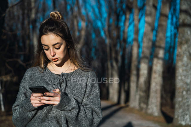 Портрет женщины в свитере с телефоном на аллее парка — стоковое фото