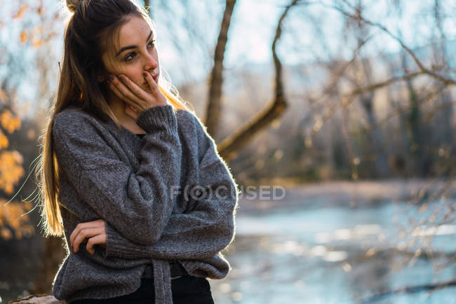 Vue latérale de la femme rêveuse en pull posant dans les bois automnaux — Photo de stock