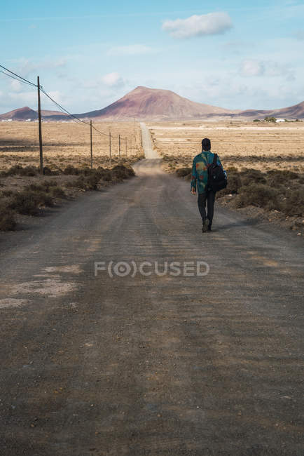 Vista trasera del hombre caminando por la carretera en el campo - foto de stock