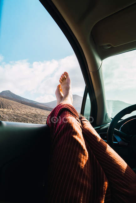 Crop pieds mâles collant par la fenêtre de la voiture sur fond de vallée de montagne — Photo de stock