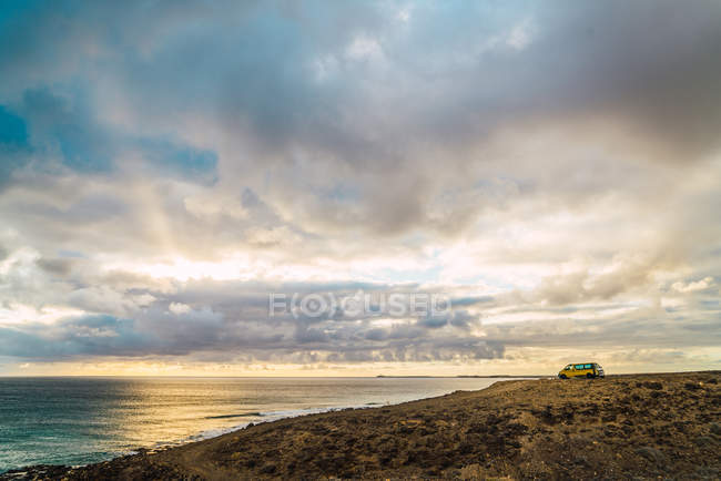 Vista panorámica a la costa nublada y furgoneta estacionada a distancia - foto de stock