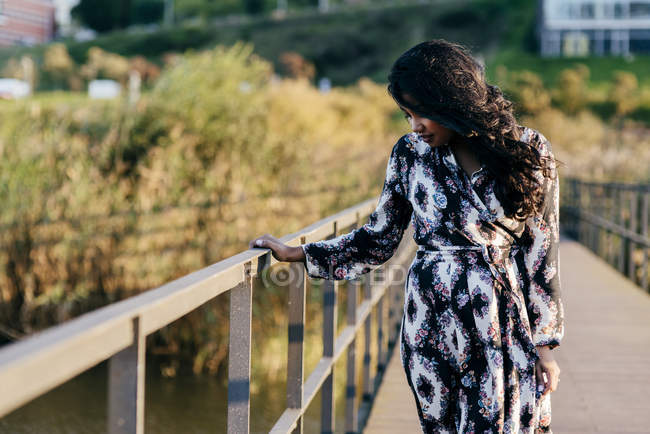 Donna con un bel vestito che cammina sul ponte e guarda giù — Foto stock