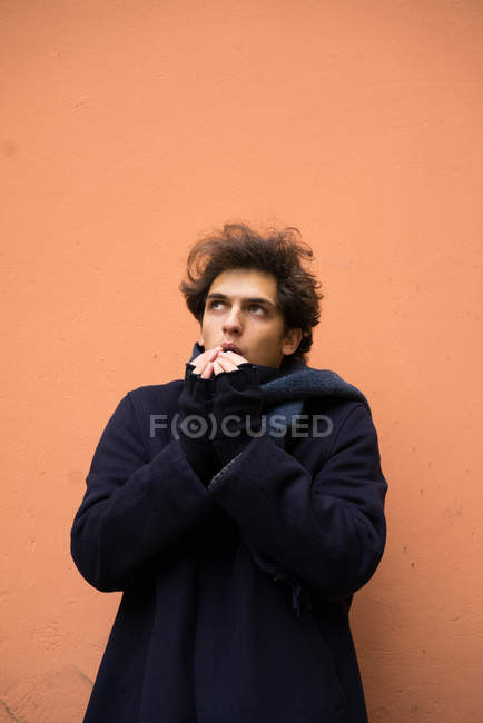 Портрет человека, согревающего руки дыханием и смотрящего на фоне оранжевой стены — стоковое фото