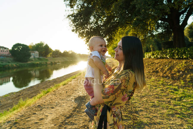 Vue latérale de la mère avec enfant sur les mains dans le parc d'été — Photo de stock