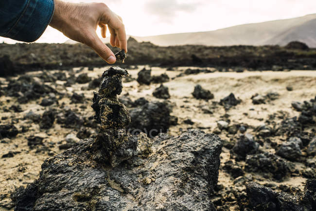 Crop male hand stacking volcanic stones in tower — Stock Photo