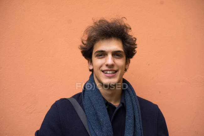 Smiling man in stylish coat looking at camera at orange wall outdoors. — Stock Photo