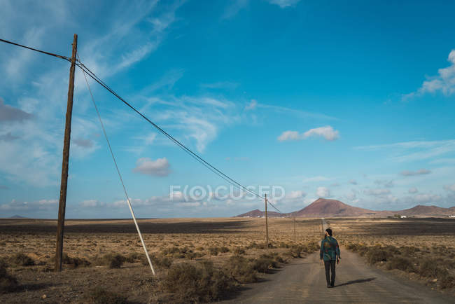 Vue arrière du touriste marchant sur la route rurale dans un champ sec — Photo de stock
