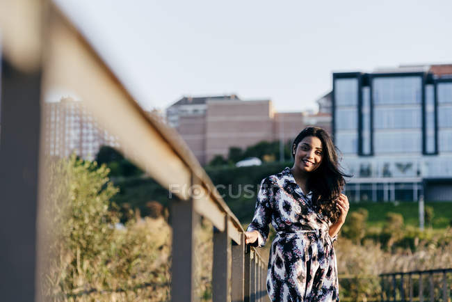 Frau in schönem Kleid posiert auf Brücke und blickt in die Kamera — Stockfoto