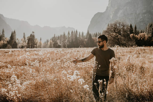 Porträt eines Mannes, der auf trockenem Gras auf einer Wiese in den Bergen wandelt. — Stockfoto