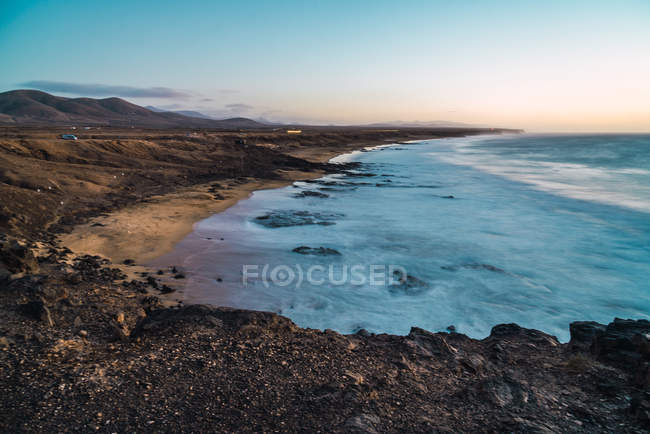 View of ocean washing rocky shoreline in sunset — Stock Photo
