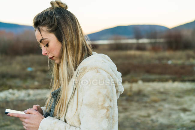 Side view of  woman browsing smartphone on background of natural landscape — Stock Photo
