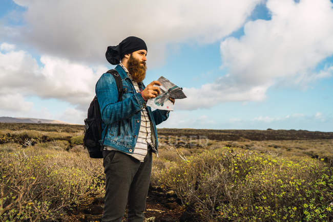 Seitenansicht eines Touristenmannes mit Rucksack und Landkarte in der Hand auf dem Land — Stockfoto