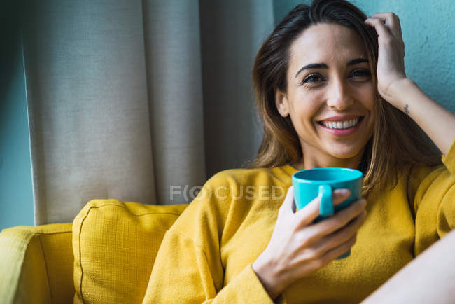 Porträt einer lächelnden Frau mit Tasse am Sessel — Stockfoto