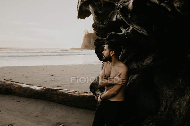 Hemdloser Mann posiert mit Koffer am Strand — Stockfoto