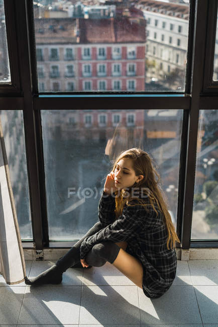 Vista de ángulo bajo de la mujer sentada en el suelo por ventana - foto de stock