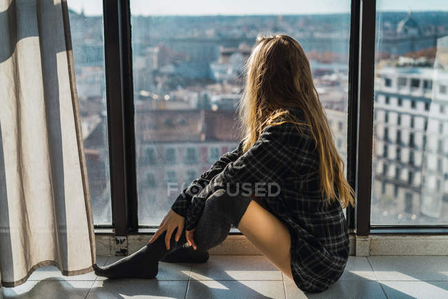 Вид збоку жінки, що сидить на підлозі біля вікна і дивиться в сторону — стокове фото