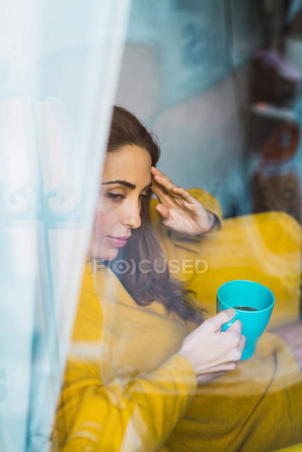 Porträt einer verträumten Frau mit Tasse hinter Glas — Stockfoto