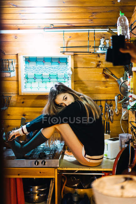 Vue latérale de la fille provocatrice posant sur le comptoir de la cuisine et regardant la caméra — Photo de stock