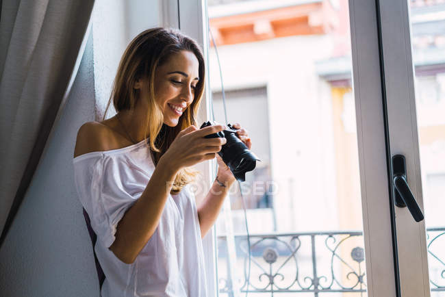 Вид сбоку улыбающейся женщины, наблюдающей за съемками на камеру из окна дома — стоковое фото
