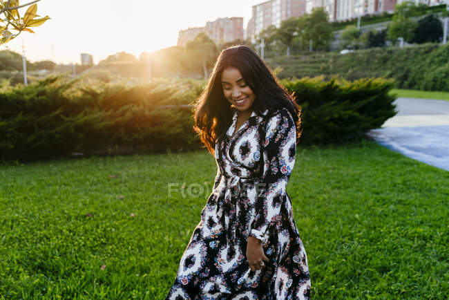 Portrait de femme gaie en robe marchant sur la pelouse ensoleillée au parc — Photo de stock