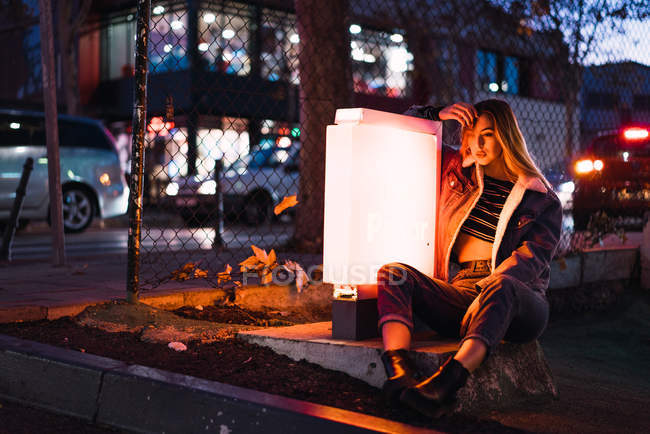 Modelo joven sentado cerca de la luz de la lámpara al aire libre en el césped y posando - foto de stock
