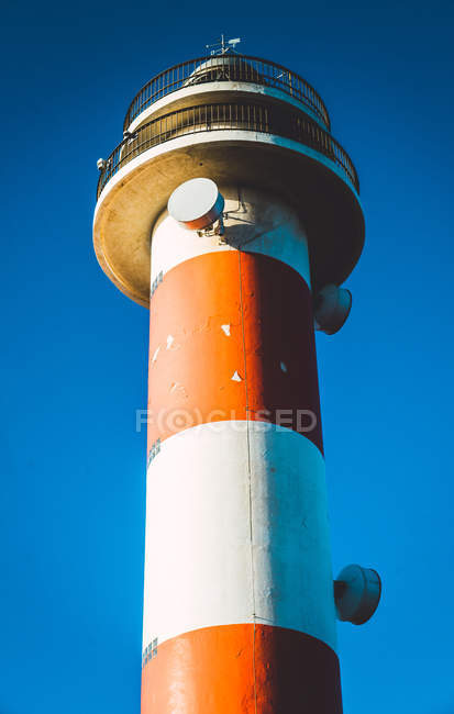 High angle view of striped red and white lighthouse on vivid blue sky in sunlight. — Stock Photo