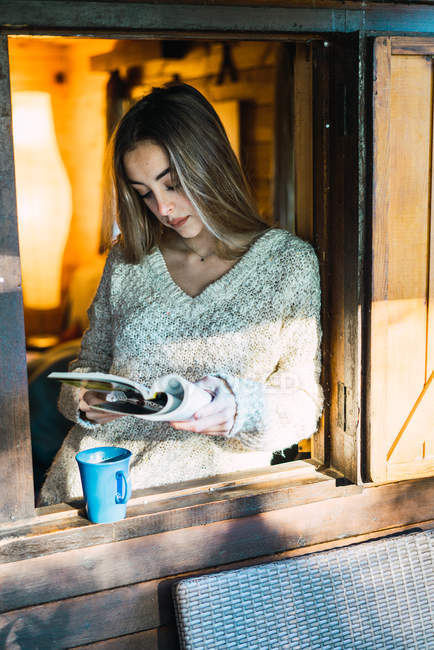 Retrato de niña con libro y café en ventana - foto de stock