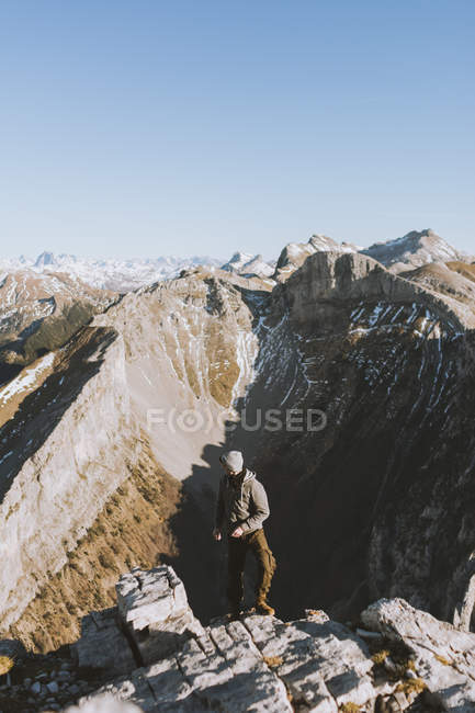 Jovem posando na borda da encosta das montanhas com fundo de cumes à luz do sol . — Fotografia de Stock