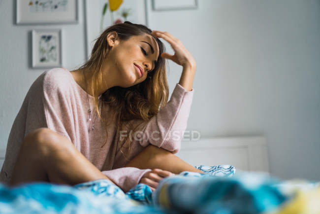 Mujer joven sentada y relajada en la cama - foto de stock