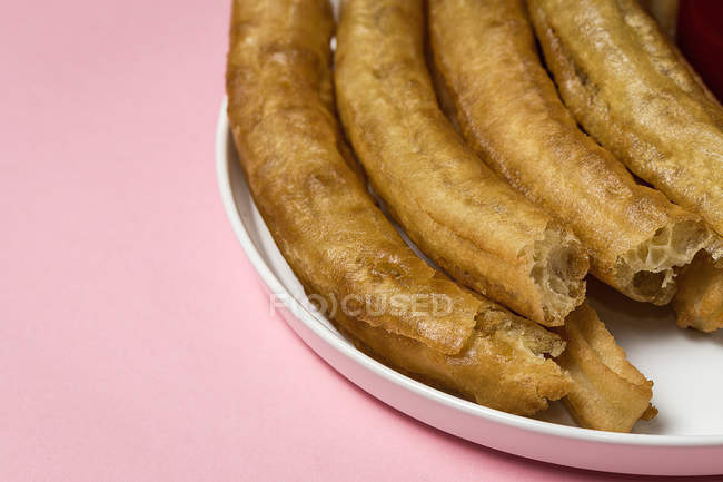 Immagine ritagliata di churros spagnoli in piatto su rosa — Foto stock