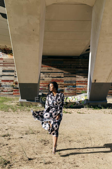Mulher de vestido bonito andando sob ponte e olhando para longe — Fotografia de Stock