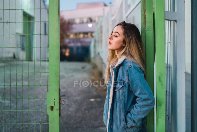 Side view of young woman leaning on fence at street scene — Stock Photo