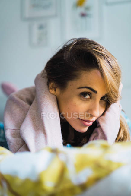 Jeune femme couchée au lit et regardant la caméra — Photo de stock