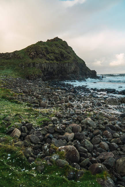 Paisaje vista a la colina verde y piedras a orillas del mar - foto de stock