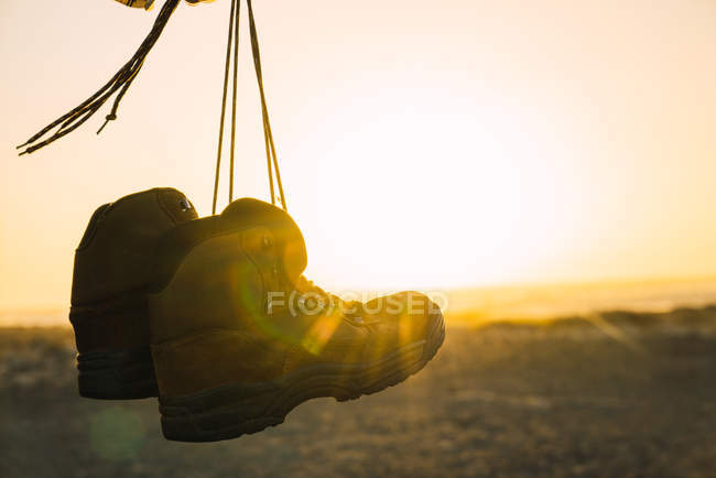 Hanging trekking boots on background of sunlit desert landscape — Stock Photo