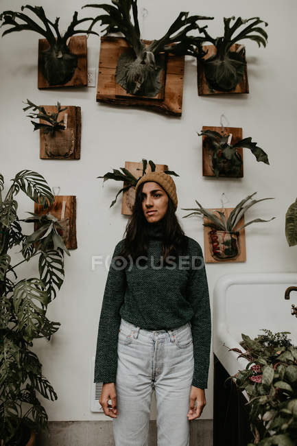 Vista frontal de la mujer de pie en invernadero en el fondo de la pared con plantas en maceta - foto de stock