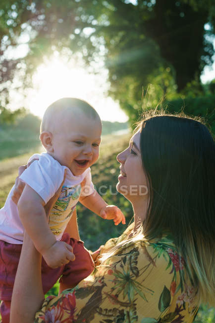 Vista lateral de la madre con el niño en las manos en el parque - foto de stock