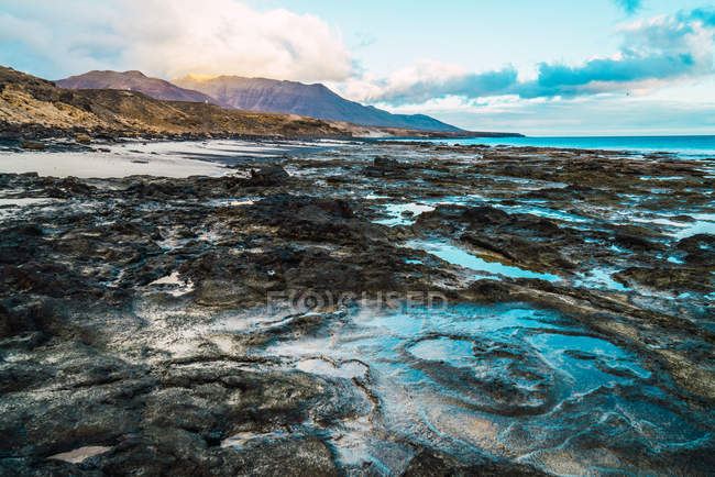 Landschaft der Meeresküste mit schmutzigen rauen Formationen vor dem Hintergrund des Himmels und der Berge. — Stockfoto