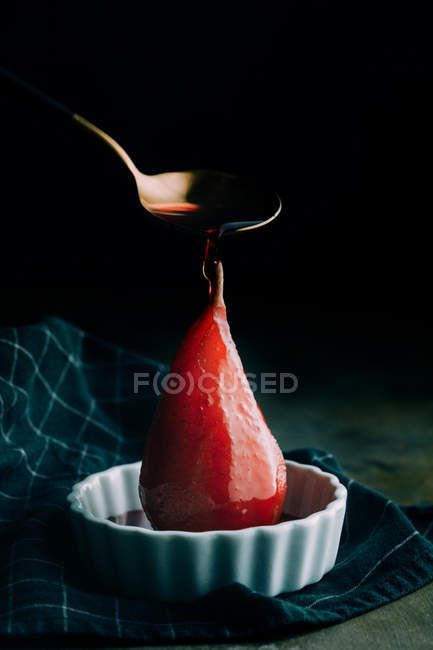 Löffel gießt pochierte Birne in weiße Keramikschüssel — Stockfoto