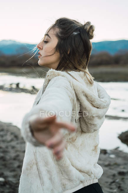 Side view of girl holding hands apart in wind on background of natural landscape. — Stock Photo