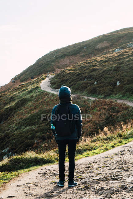 Visão traseira do turista caminhando no caminho na ensolarada colina — Fotografia de Stock