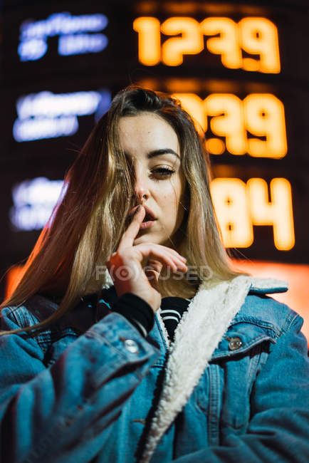 Visão de ângulo alto de loira na jaqueta de ganga segurando o dedo nos lábios na cena de rua da noite — Fotografia de Stock